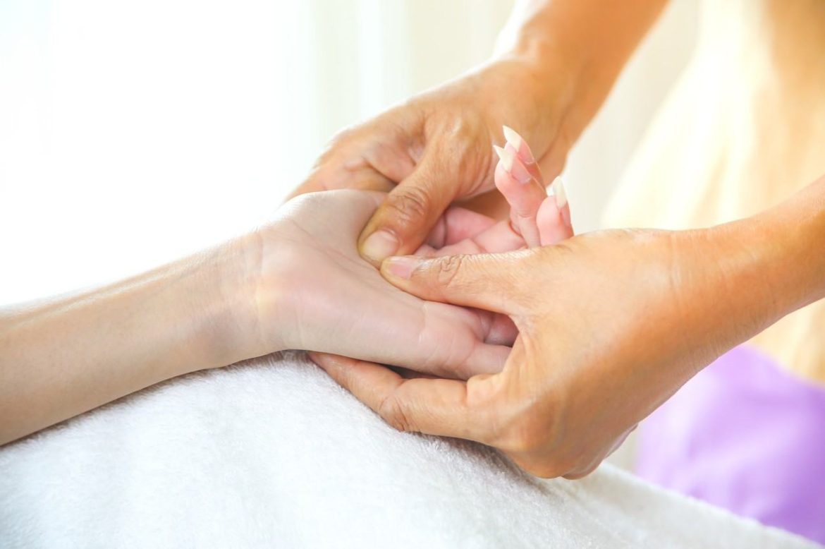 Praticienne effectuant un massage acupression sans aiguilles sur la paume de la main d’une personne.